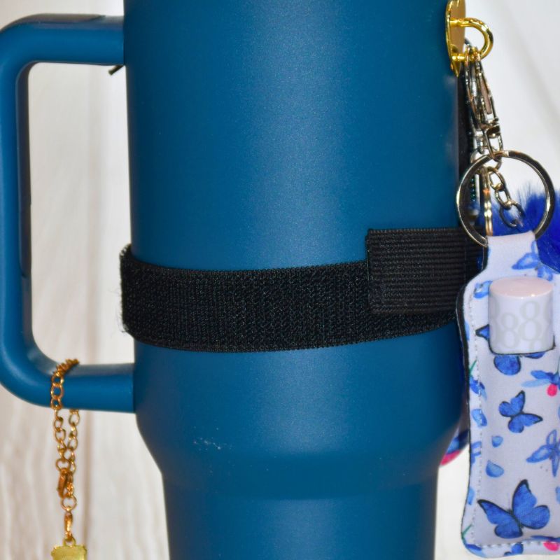 Blå sommerfugl veske festet på en blå termokopp. Her ser du baksiden hvordan den er festet med borrelåsen rundt termokoppen.