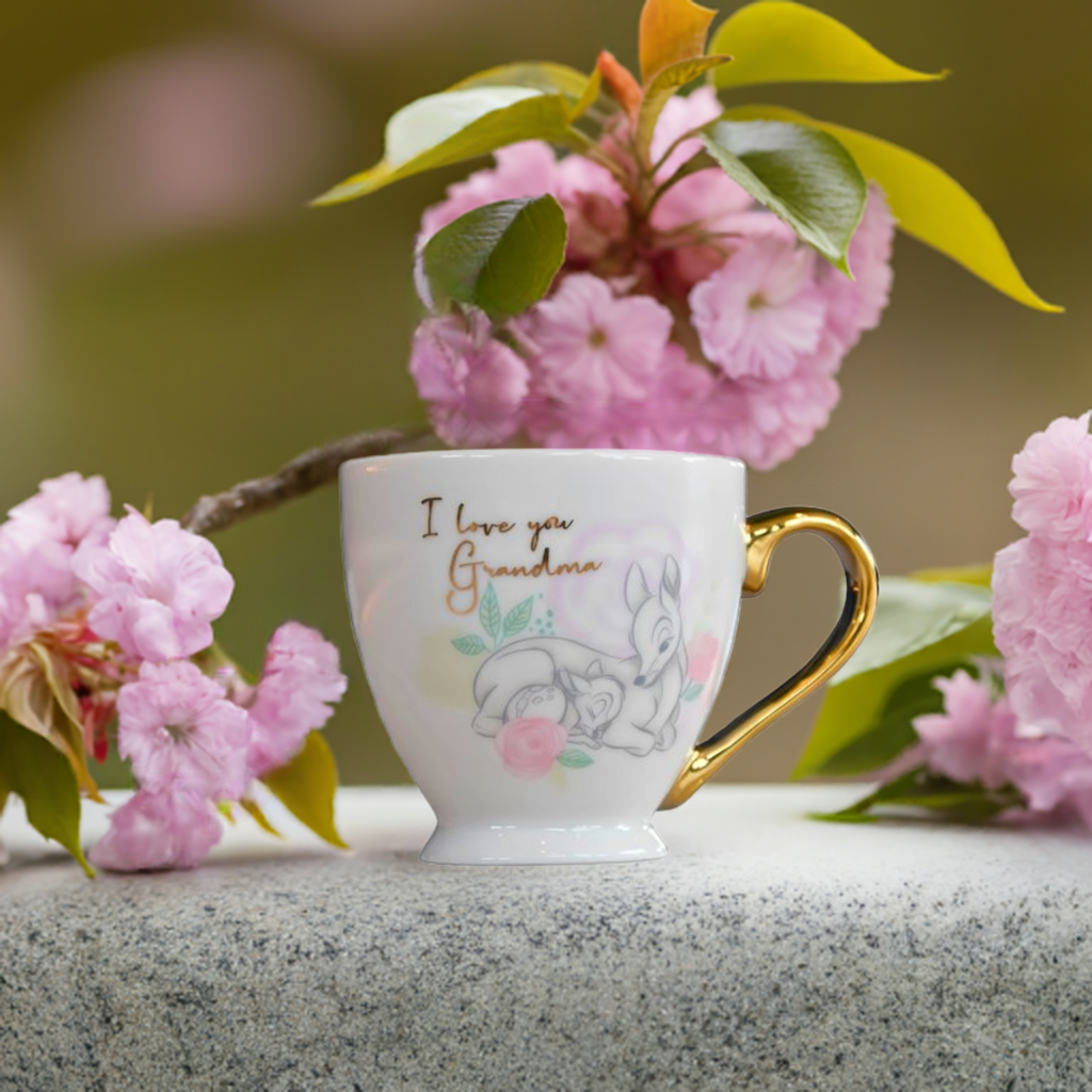 En kopp fra Disney med bambi motiv og gullhåndtak med teksten I love you grandma. Denne koppen er en kjærlighetserklæring til din bestemor, og passer perfekt som en julegave eller bursdagsgave. Koppen er plassert på en steinflate med rosa blomster rundt koppen.