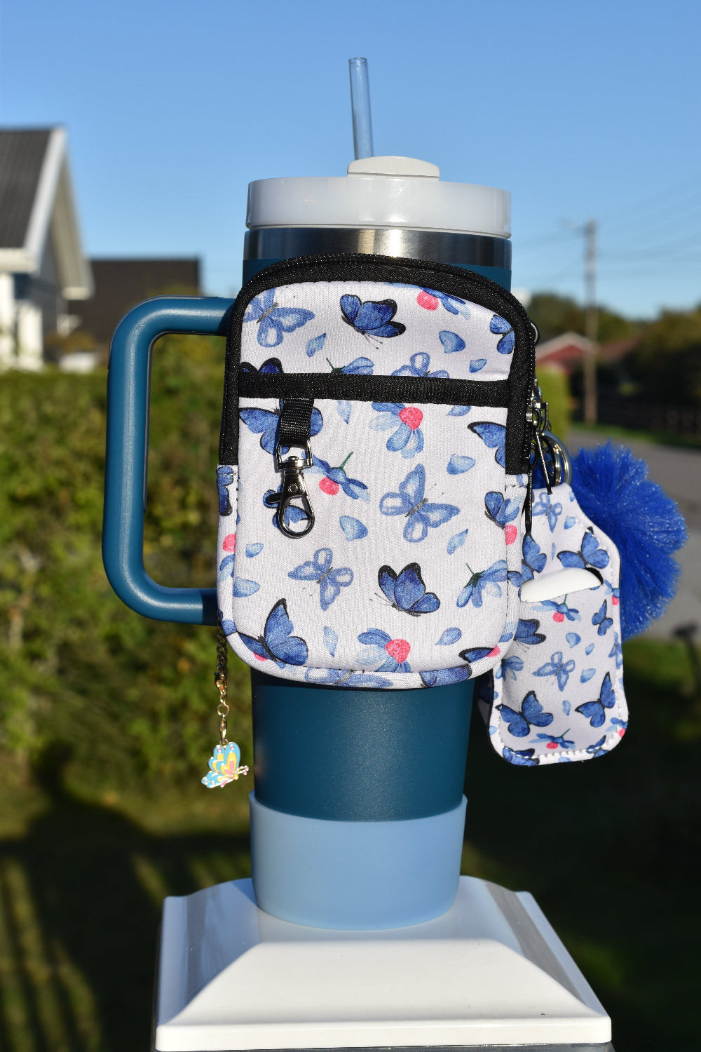 Blå termokopp som er pyntet opp med den praktiske ryggsekken og veske til airpods. Veskene har mønster med blå sommerfugler. Perfekt når man er på farten.