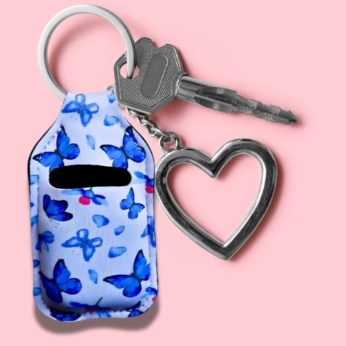Veske beskyttelse til airpods med sommerfugl motiv. Her henger den på en nøkkelklype sammen med en nøkkel og et hjerte.