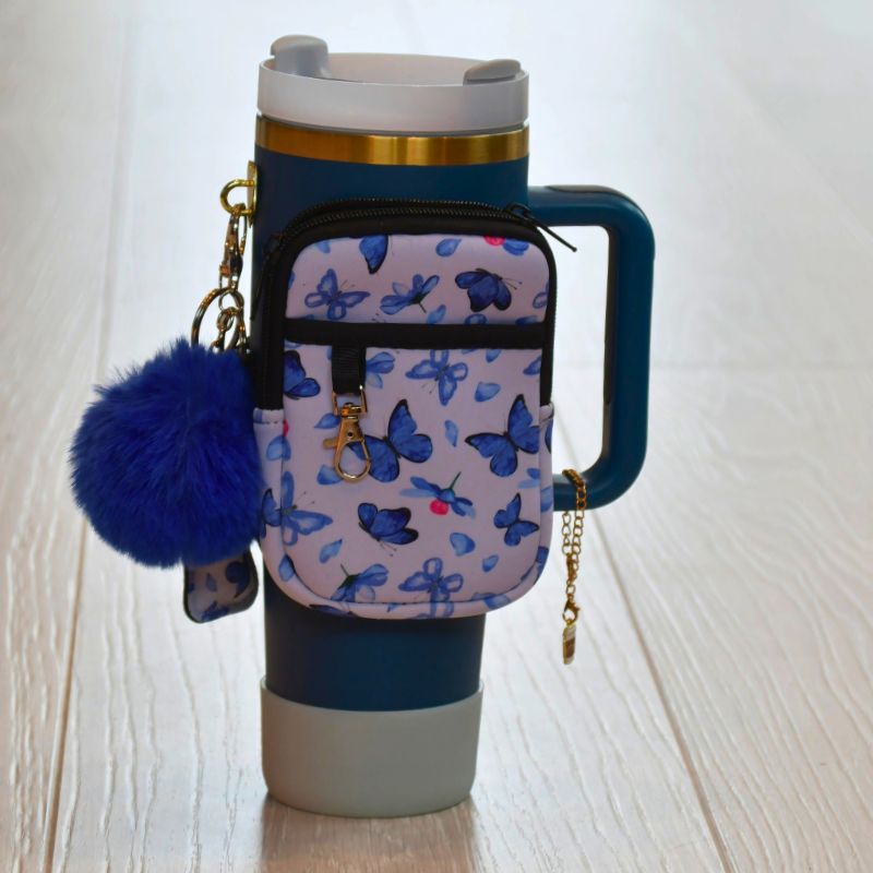 Blå sommerfuglveske i bruk på en blå termokopp med gullkant.
