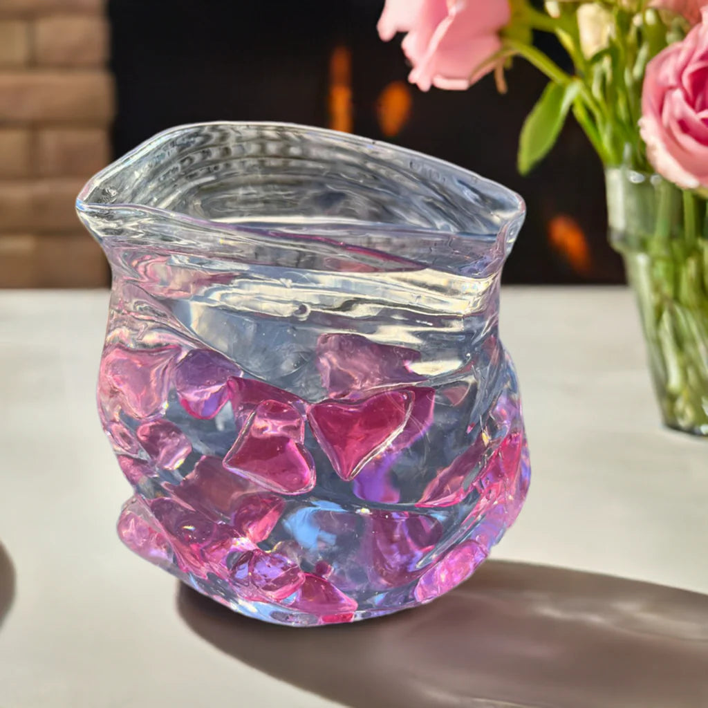 En glassbolle som er formet som en åpnet pose. Glassbollen er fylt opp med vann og rosa hjerter.