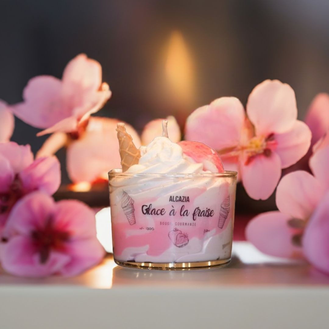 Et håndlaget duftlys som ser ut som en deilig dessert med is. Rosa blomster ligger rundt duftlyset