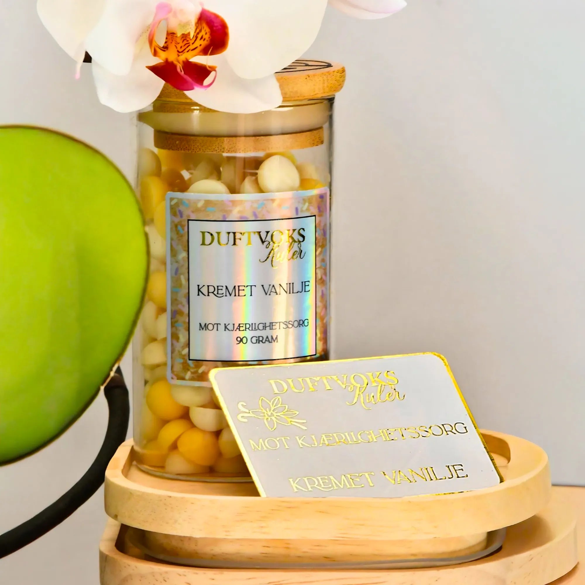 Duftvoks med duft av kremet vanilje. En duft som skal lindre følelsen av kjærlighetssorg. Et følelskort som beskriver duften i hvit med gullskrift står foran glasset med duftvoksen. Duftvoksen er små kuler, som til sammen rommer 90 gram i et glass med trelokk.