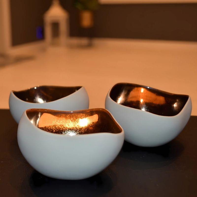 Telysholdere med telys i utstilt i stuen. Fargen er kremhvit og bronse. Disse kommer pakker med 3stk og gir hjemmet ditt et luksuriøst inntrykk. Disse er håndlaget i Frankrike så hver holder er helt unik. Interiør som varer og lyser opp hverdagen.