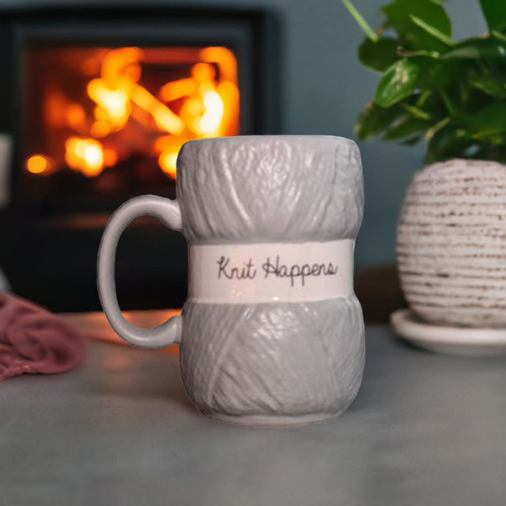 Grå strikkekrus på bordet forran peisen. På koppen står det "knit happens".
