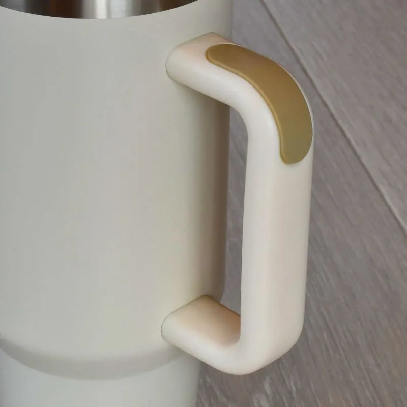 Nærbilde av håndtaket på en beige termokopp. Håndtaket har silikon som gir et behagelig og ergonomisk grep. Tumbler rommer 1,2 liter og holder drikken kald gjennom hele dagen. Kan også brukes med varm drikke.