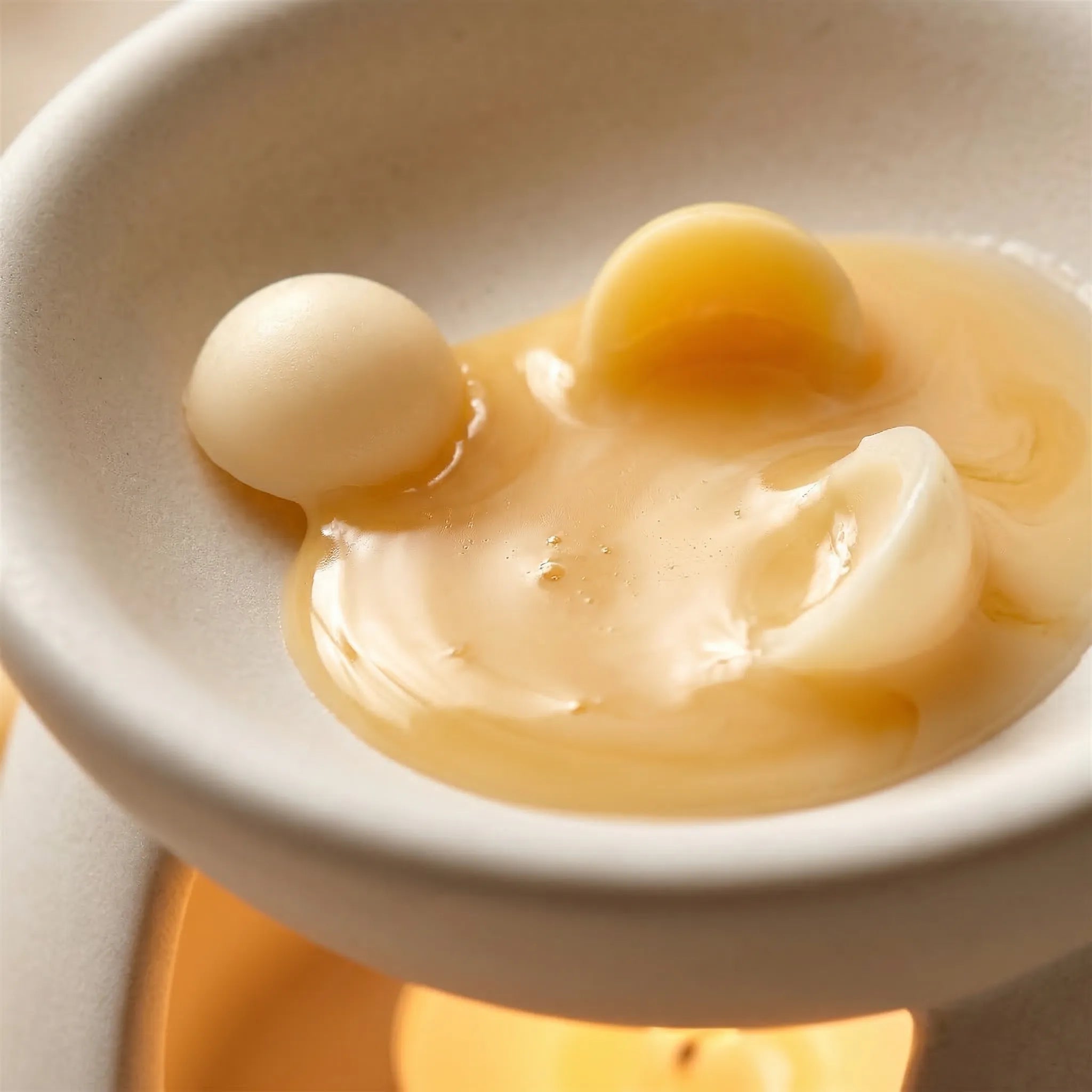 Smeltet duftvoks kuler. Her kan man se de ligger i en duftbrenner. Det er et telys i duftbrenneren som varmer opp de håndlagde duftvokskulene som ligger på toppen. Nå fyller duften av kremet vanilje hjemmet, og det er bare å lene seg tilbake mens duften sprer seg i rommet.