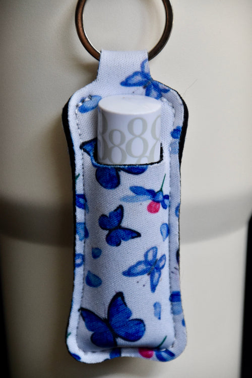 en veske til lipsyl eller leppepomade med sommerfugl motiv som er festet på en beige termokopp. Kan også festes på sekker, nøkkelringer, jakke osv. Lipsyl eller leppestilt lett tilgjengelig.