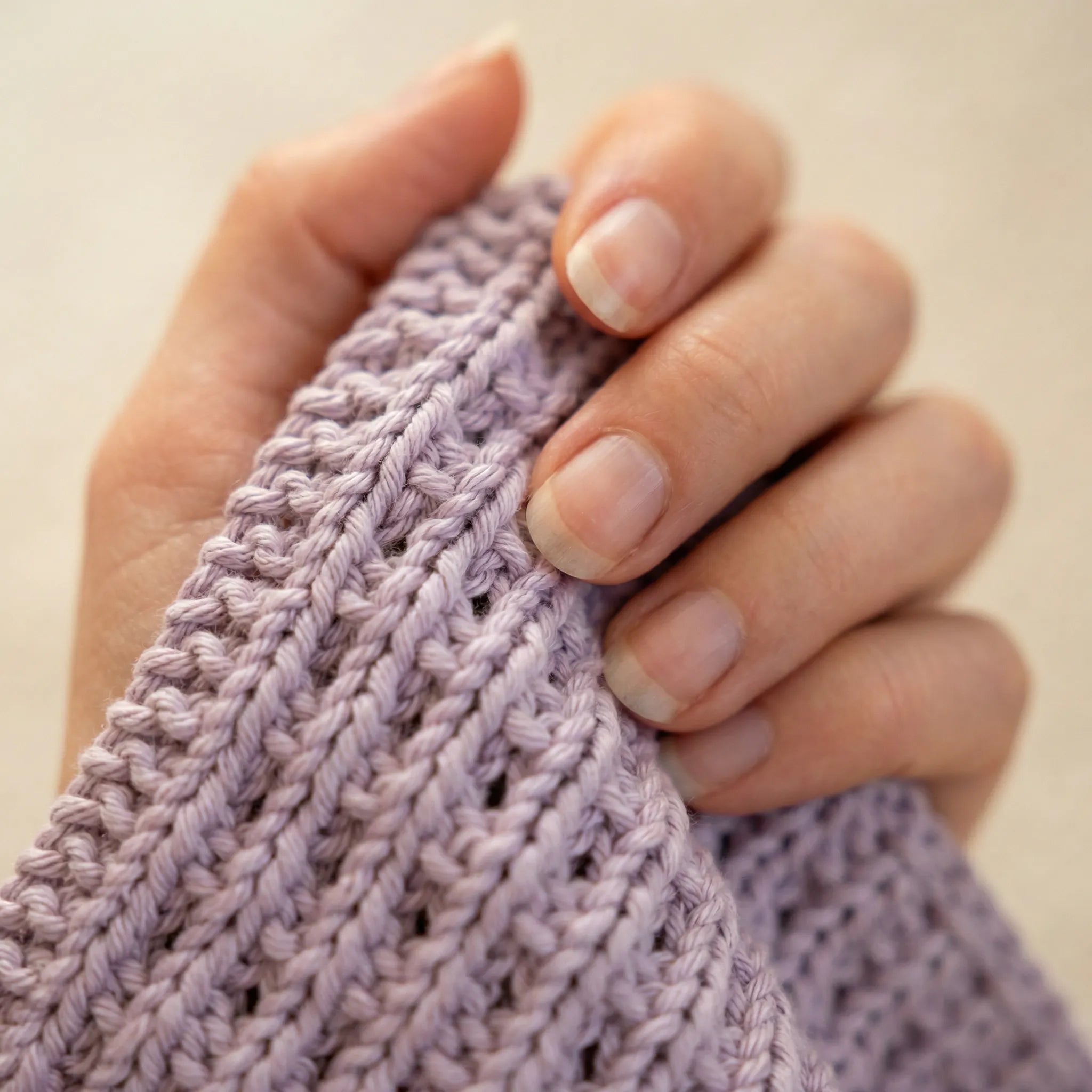 Kjøkkenklut / vaskeklut i fargen lilla. Her er nærbilde av kluten som er håndstrikket av mamma. Man ser godt detaljene som mønsteret den er strikket i og en hånd som holder vaskekluten i hånden sin, klar for å bli brukt enten på kjøkkenet eller på badet, det er helt opp til deg. Perfekt som gave og disse kommer i 6 forskjellige farger.