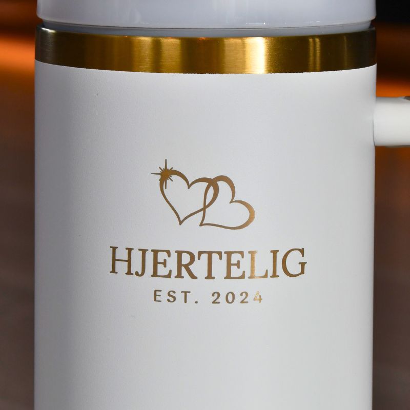 Nærbilde av logo og gullkant på hvit termokopp