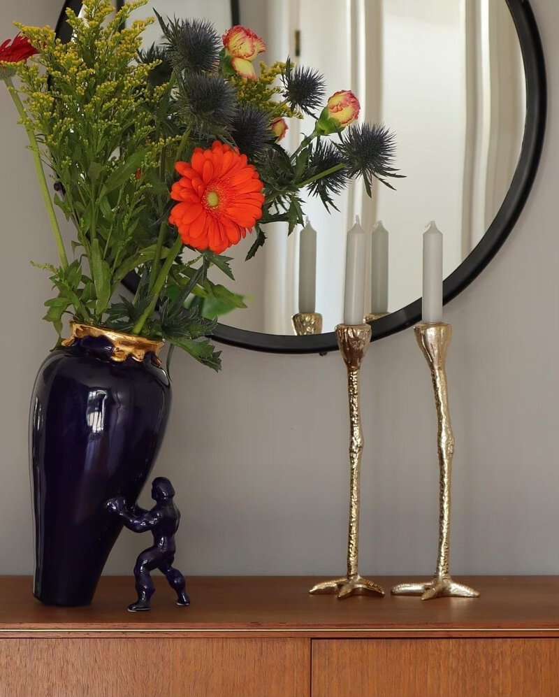 Long legs strutse bein som står på en benk vesidenav my superhero vase og et speil i bakgrunnen.