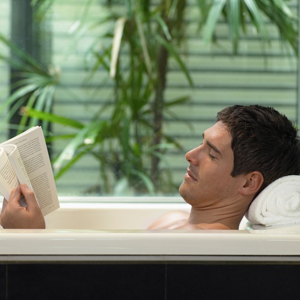 En mann som ligger i et badekar og leser bok. Et illustrasjonsbilde for å vise at du må sette av tid og ta vare på deg selv.