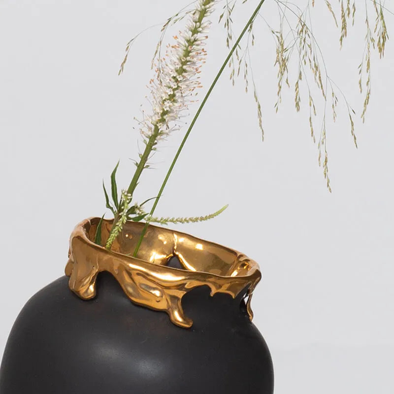Bilde av toppen av en sort vase. Toppen av vasen er 24 karat gullbelagt med en flytende effekt. Det står noen strå i vasen