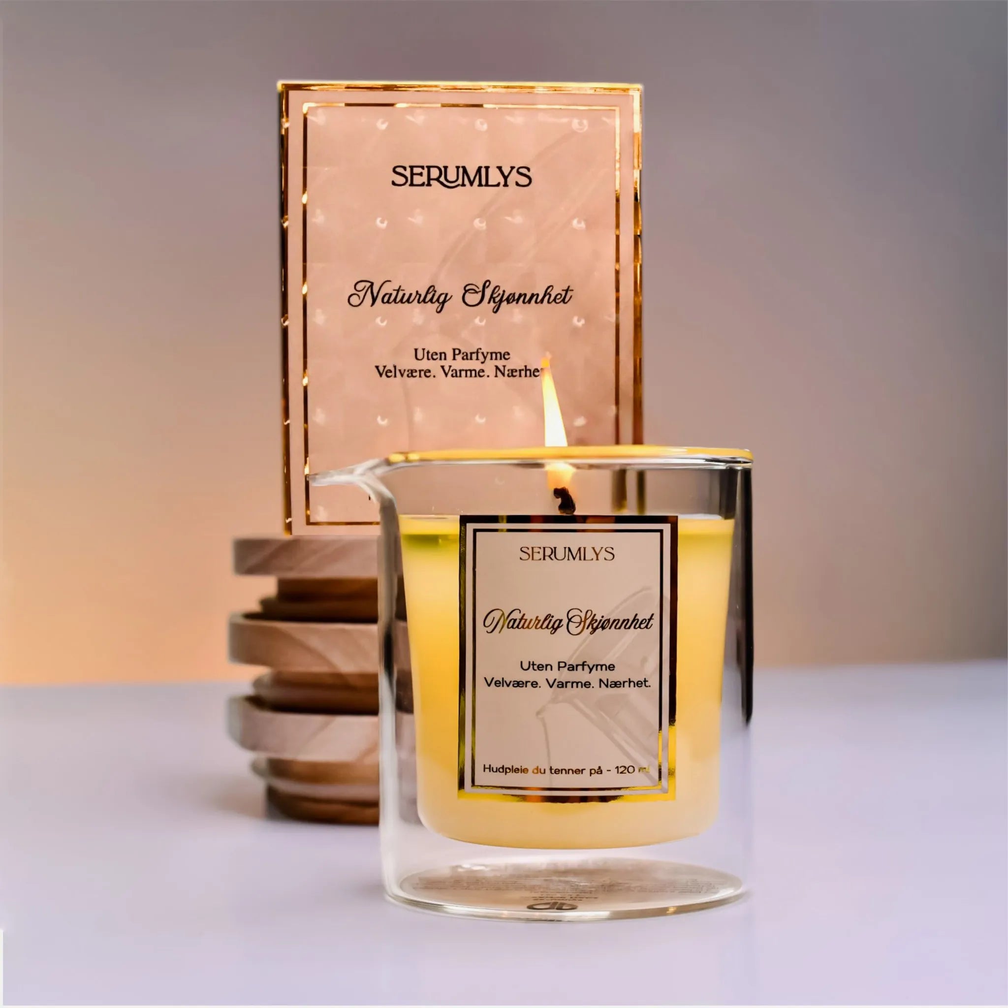 Et glass med lys som er tent. Blandingen smelter til et pleiende kroppsserum som trekker raskt inn i huden. Gir næring, glød og fuktighet. Laget for å gi seg selv en følelse av velvære. I bakgrunnen står produktesken i beige farge og skinnende gulldetaljer.