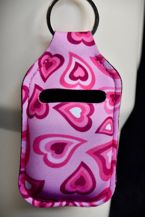 Rosa veske med hjerte design til airpods eller andre ørepropper. Den er festet på en beige termokopp