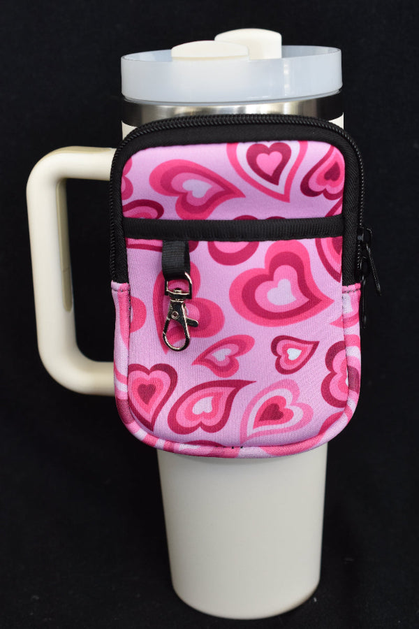 En liten ryggsekk med hjerte motiv som er festet rundt en beige termokopp.