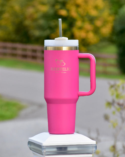 Tumbler med sugerør og håndtak i rosa farge med gullkant og logo. Her står den ute og man ser de nydelige gulldetaljene som lasergravert hjertelig logo og med gull hjerter over. En nydelig drikkeflaske som garantert vil komme godt med. Varm eller kald drikke hele dagen! Praktisk og luksuriøst utsende.
