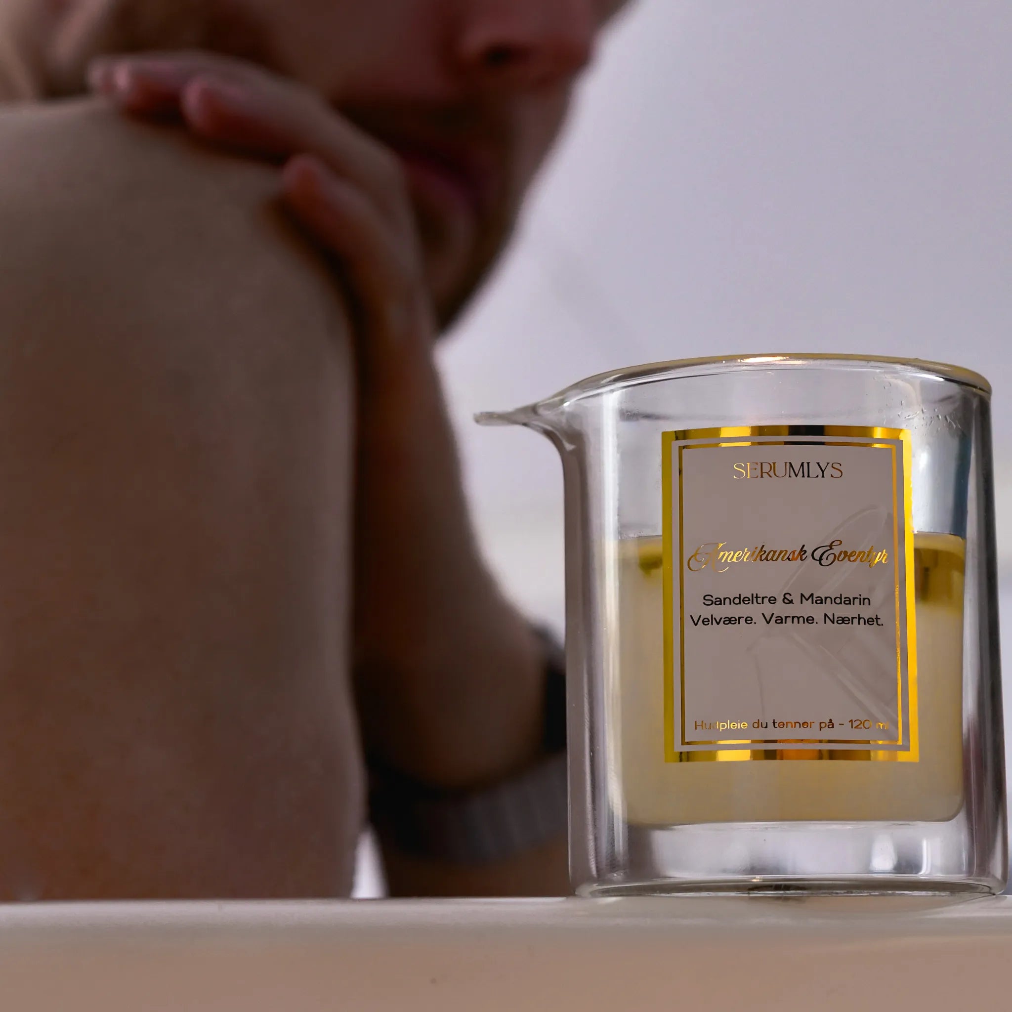 Serumlys med duft av sandeltre og mandarin. En mann er i bakgrunnen som smører inn skulderen sin.