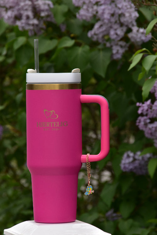Et smykke med sommerfugl motiv som viser hvordan det ser ut når den er festet på en rosa termokopp med sugerør og håndtak med gullkant
