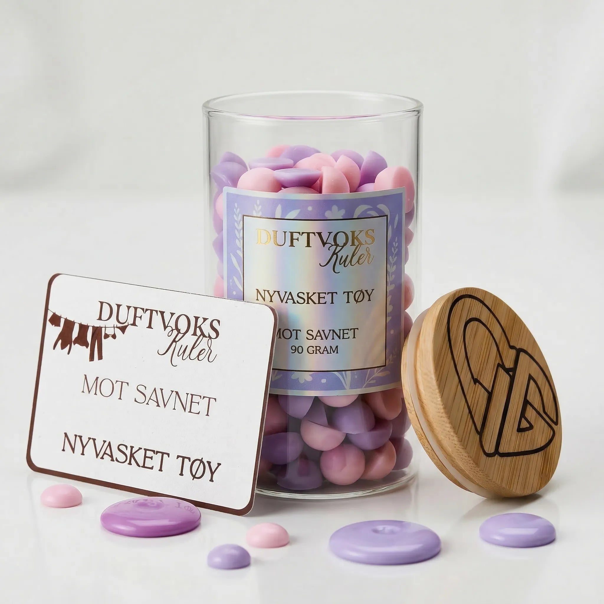 Håndlaget duftvoks kuler i fargen lilla og rosa. Disse voks kulene fyller huset ditt med en herlig rein duft av nyvasket tøy og nyvasket hus. Blomster lukter man forbinder med reint. Denne varianten er dedikert til de som savner noen llitt ekstra. Duftvoks kulene kommer i en nydelig glasskrukke med bambuslokk som man kan gjennbruke.
