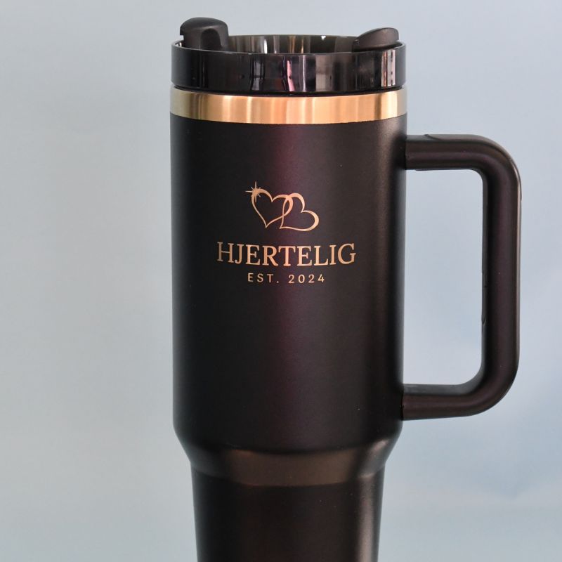 Svart termokpp med gull detaljer og nærbilde av logoen hjertelig. Sammen med 2 gullhjerter over.