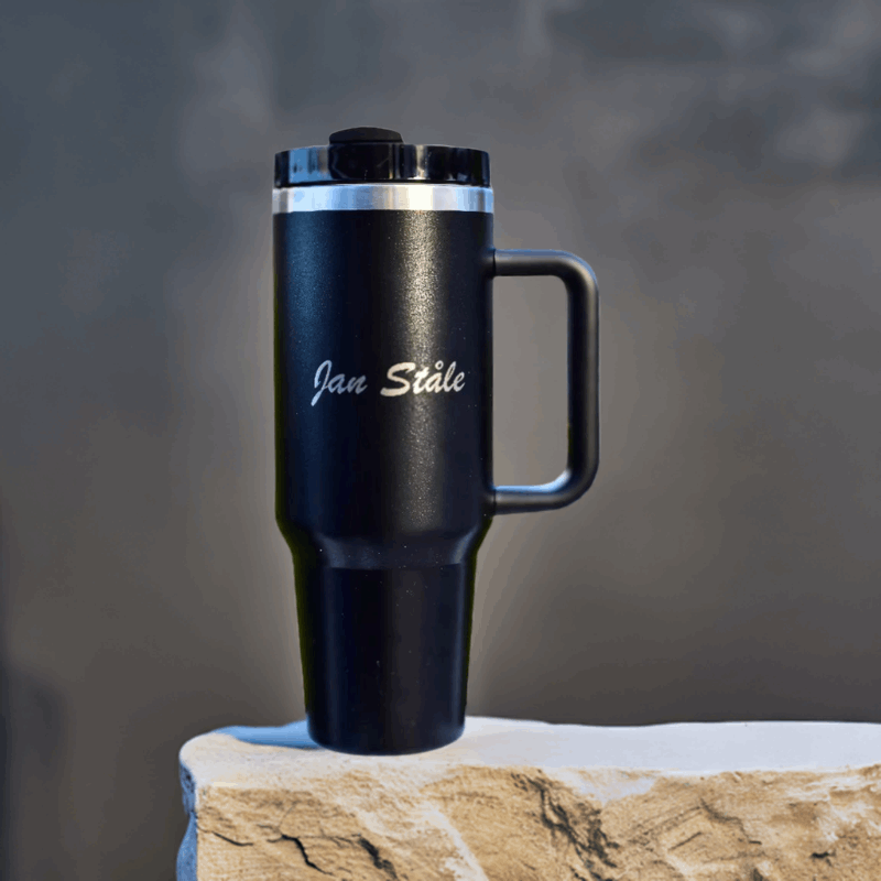 Svart termokopp med lasergravering utstilt på en stein