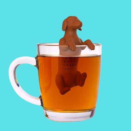 Tesil som ser ut som en hund som holder hodet over det varme vannet. Hunden henger på kanten av koppen.