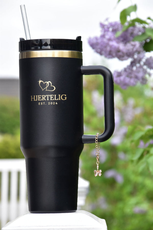 Svart termokopp med gullkant og rosa smykke i stein