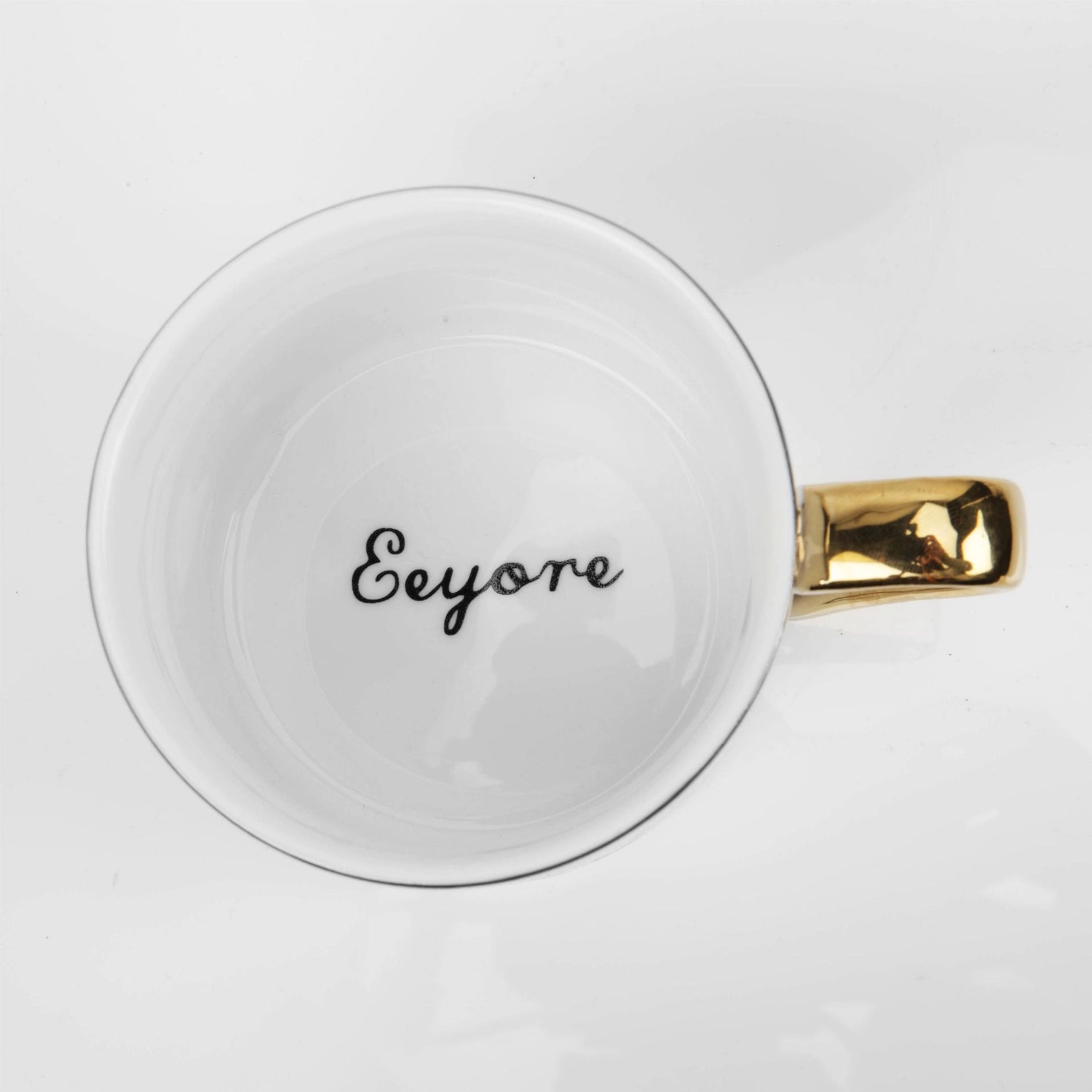 Tussi kopp med skrift i bunnen inni. Her ser man også det nydelige gullhåndtaket til kaffe koppen. Hvit keramikk krus ovenifra.