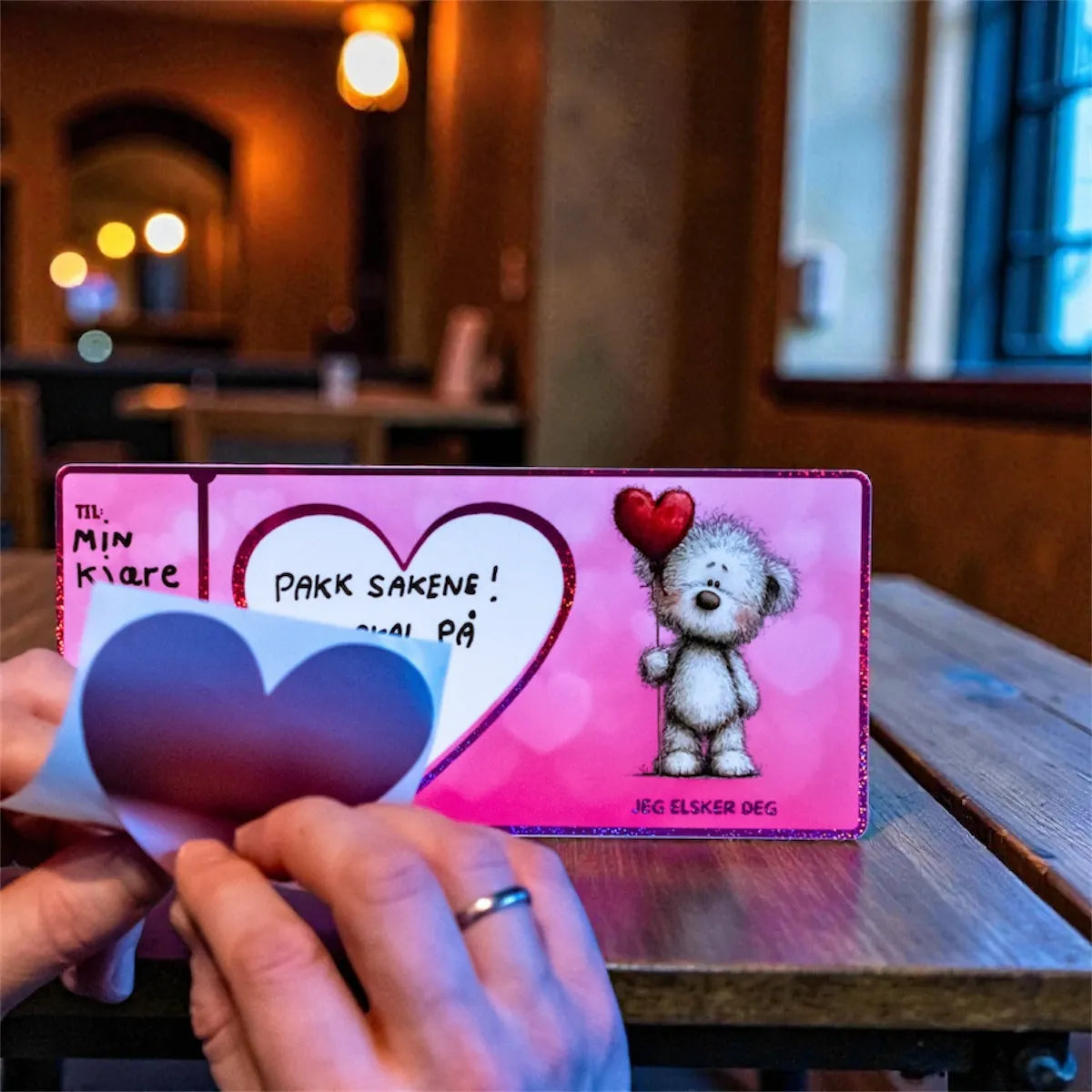 Her ser man at valentineskortet er skrevet på. Overraskelsen står nå på kortet, og da er det bare å klistre skrape klistremerke over teksten. På bilde taes klistremerke av klistremerke papiret, for så å feste teksten så den blir skjult. En romantisk og fin måte å gi bort den perfekte valentinesgaven på!