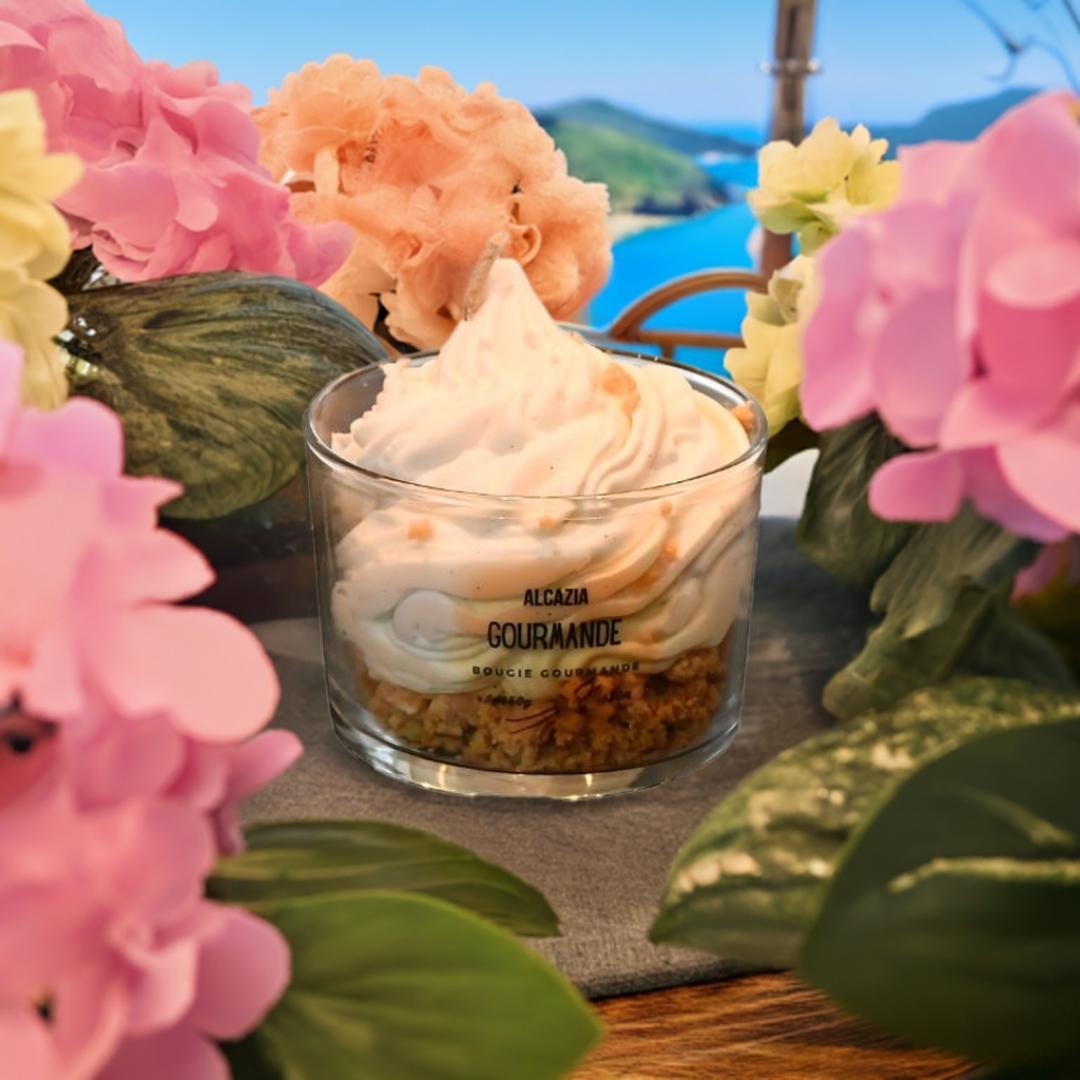 Håndlaget duftlys med lukt av vanilje som er omringet av blader og blomster. I bakgrunnen ser du en innsjø og en strand.