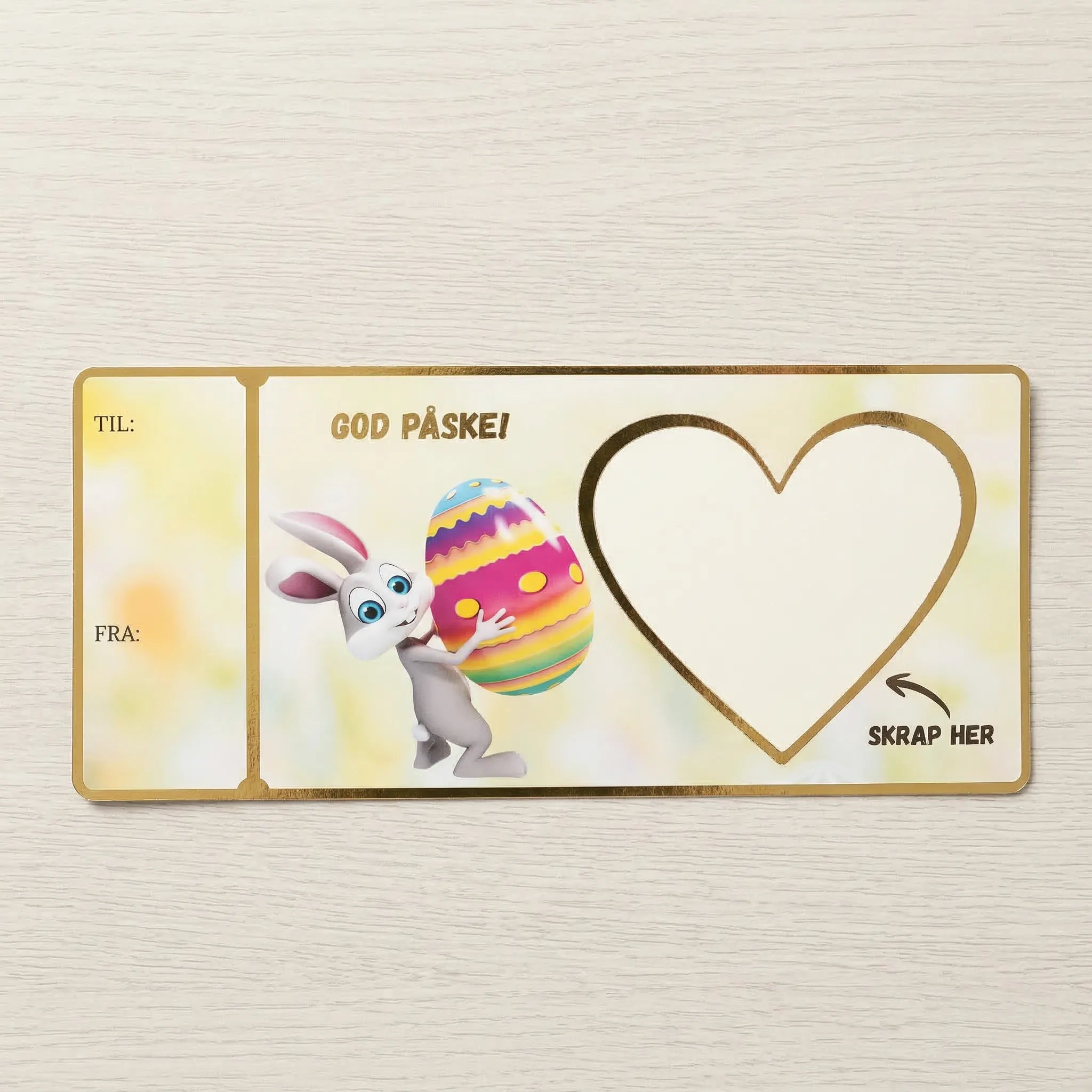 Et kort med skrapefelt. Påske design med kanin som løfter et stort påskeegg. Skriv inn gaven du ønsker å gi i det hvite feltet. Så fester du et klistremerke med skrapefelt over teksten som følger med kortet. Håndlaget i Norge. Gullfolierte detaljer rundt kantene og tekst. Tykt solid papir med levende farger.