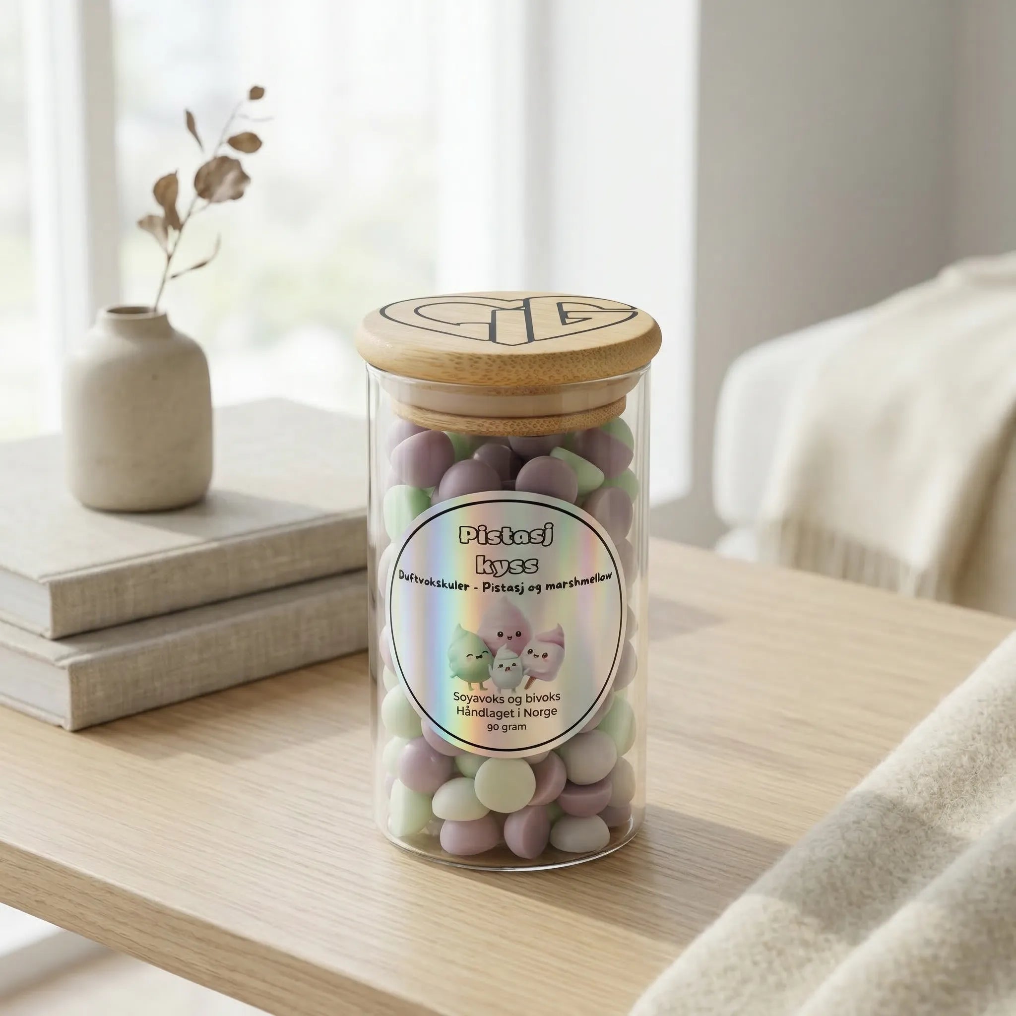 Et glass med 90 gram duftvoks i glass med trelokk som står på et bord. Duften heter Pistasj kyss, og er en søt blanding av pistasj og marchmallows. Lys grønn og lys beige duftvokskuler som sprer god duft i rommet som varer i mange timer. Brukes sammen med en duftbrenner.