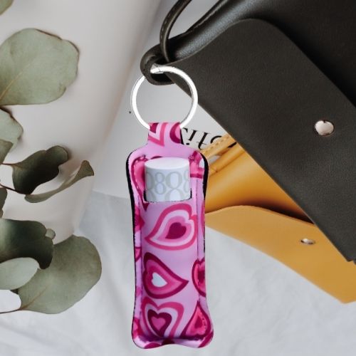 En nøkkelring til leppestift med rosa hjerter som design. Nøkkelringen er festet på en sort veske.