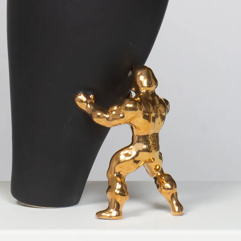Nærbilde av en superhelt i gull som støtter opp en sort vase som ser ut til å falle