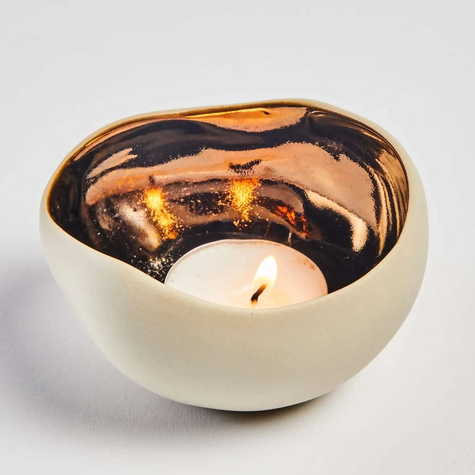 Håndlaget telysholder med en kremhvit utside og bronsefinish innvendig. Bruk alle tre sammen, eller hver for seg. Her er den ene i bruk og man kan se at bronsen får et nydelig gjennskinn når telyset er tent. Stemning og en lun atmosfære i hjemmet med håndlaget interiør fra Frankrike.