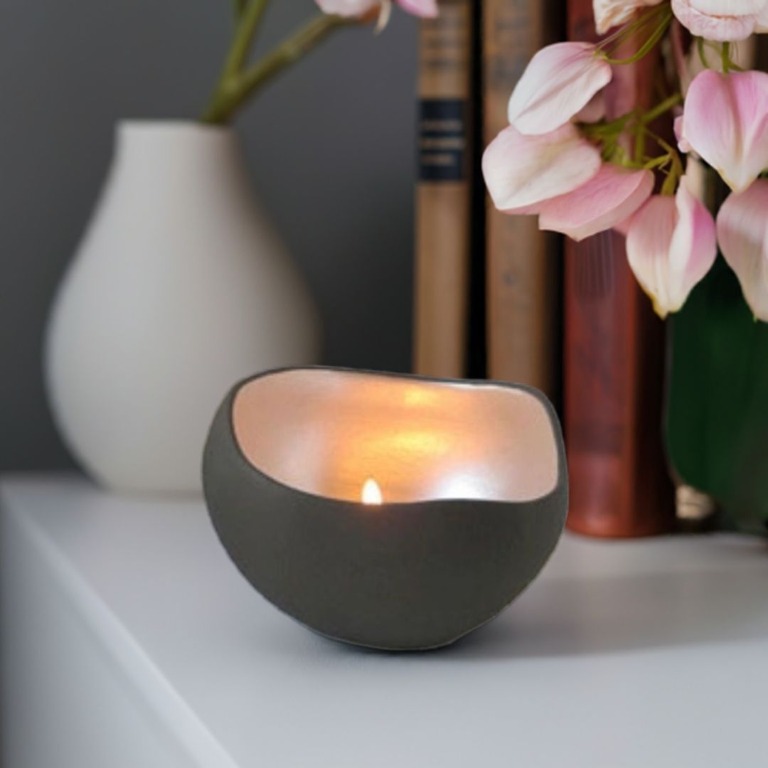 En håndlaget telysholder som står på et bord. I bakgrunnen ser du en blomsterpotte og bøker