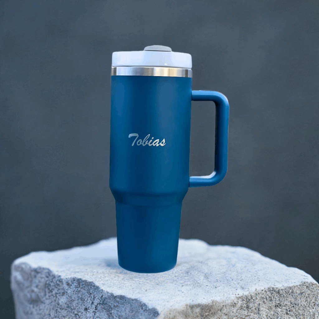 Blå termokopp med lasergravert navn utstilt på en stein. Valgfri tekst som gjør at dette er den perfekte gaveideen til noen du er glad i. Lasergraver navnet, en morsom eller omsorgsfull tekst på den. En gave som både er praktisk, omsorgsfull, personlig og full av omtanke. Skriv teksten i kommentarboksen og vi gjør resten av jobben. 