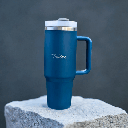Blå termokopp med lasergravert navn utstilt på en stein. Valgfri tekst som gjør at dette er den perfekte gaveideen til noen du er glad i. Lasergraver navnet, en morsom eller omsorgsfull tekst på den. En gave som både er praktisk, omsorgsfull, personlig og full av omtanke. Skriv teksten i kommentarboksen og vi gjør resten av jobben. 