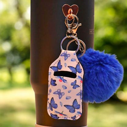 Blå veske til airpods som man foreksempel kan henges på termokoppen med krok. Den kan også henges andre plasser som på sekken, nøkkelringen eller jakken. Da har du alltid kontroll på hvor airpodsene dine er til en hver tid. Disse er håndlaget og denne har sommerfugler på seg med hvit bakgrunn og blomster. 