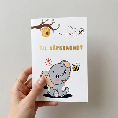 Forsiden av dåpskortet til dåpsbarnet med en babyelefant og to bier. Et tre som stikker ut med en bikubbe og gullfoliert tekst hvor det står til dåpsbarnet. Kortet er printet på høykvalitets matt fotopapir, noe som gjør det veldig enkelt å skrive det man måtte ønske inni kortet. 