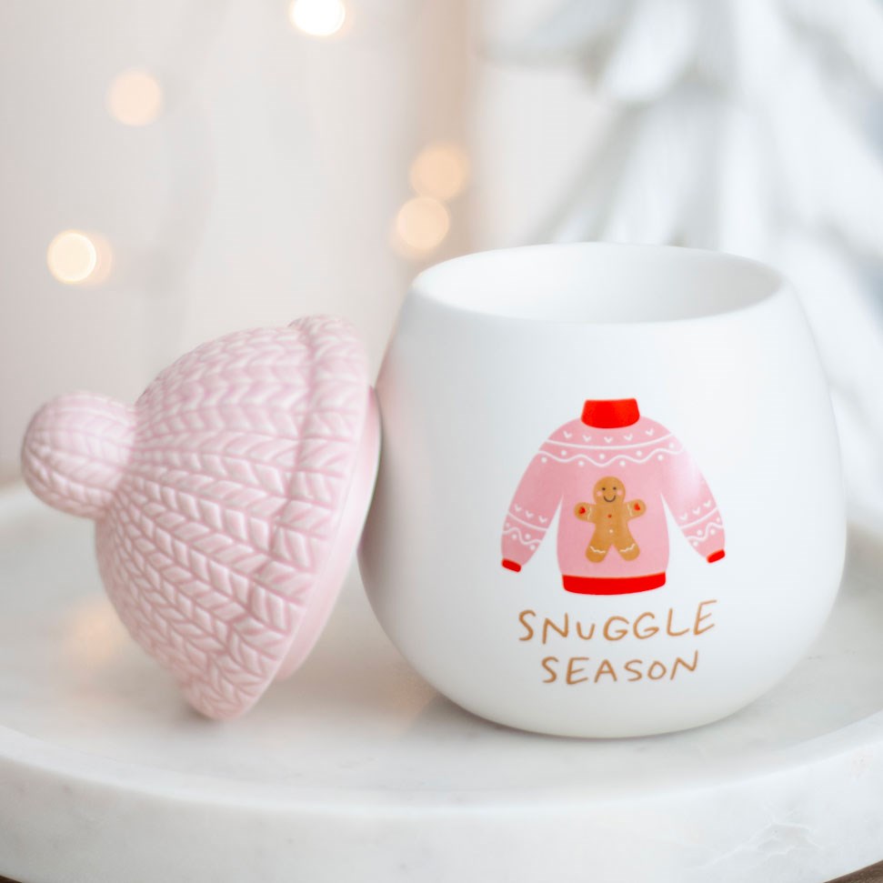 En hvit duftbrenner med et design av en rosa strikkegenser med teksten Snuggle season. Lokket er formet som en rosa strikkelue og er plassert ved siden av selve duftbrenneren. Sprer herlig duft i rommet og vil være en nydelig del av din julepynt. Passer perfekt som en julegave til noen man er glad i.