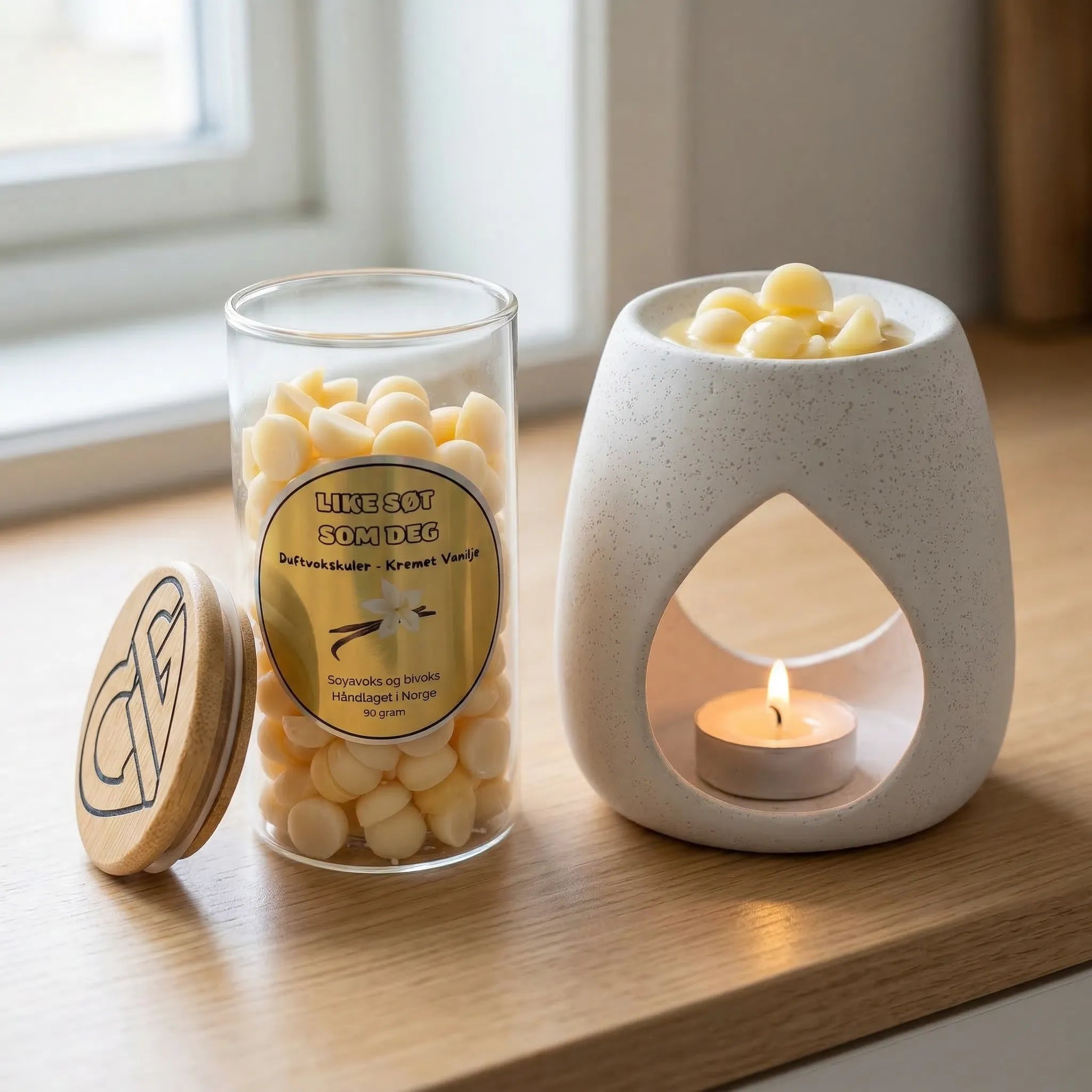 Duftvokskuler i lys gul farge i glass med en duftbrenner ved siden av. Glasset innehodler 90g duftvoks. Noen vokskuler smelter i duftbrenneren og sprer herlig myk duft av kremet vanilje ut i rommet. Voksen er håndlaget i norge med soyavoks og bivoks.