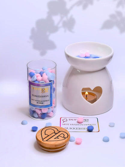 Duftbrenner i bruk med telys i hjerteåpningen. Duftvoks kulene i fargen blå og rosa ligger rundt og kortet som følger med om hverdagspress. Glasskrukken er åpen og har en nydelig ettikett med hvor det står duftvokskuler i gullfarge. Eksklusiv gave å gi til noen du bryr deg om. 