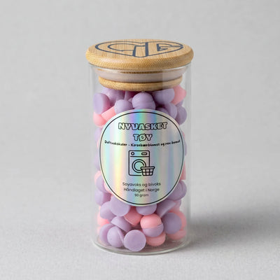 Håndlaget duftvoks som lukter nyvasket tøy. Laget med soyavoks og bivoks. Små kuler av voks i lilla og lys rosa farge. Brukes sammen med en duftbrenner som smelter vokskulene, slik at rommet fylles med nydelig duft. Glasset inneholder 90g voks.