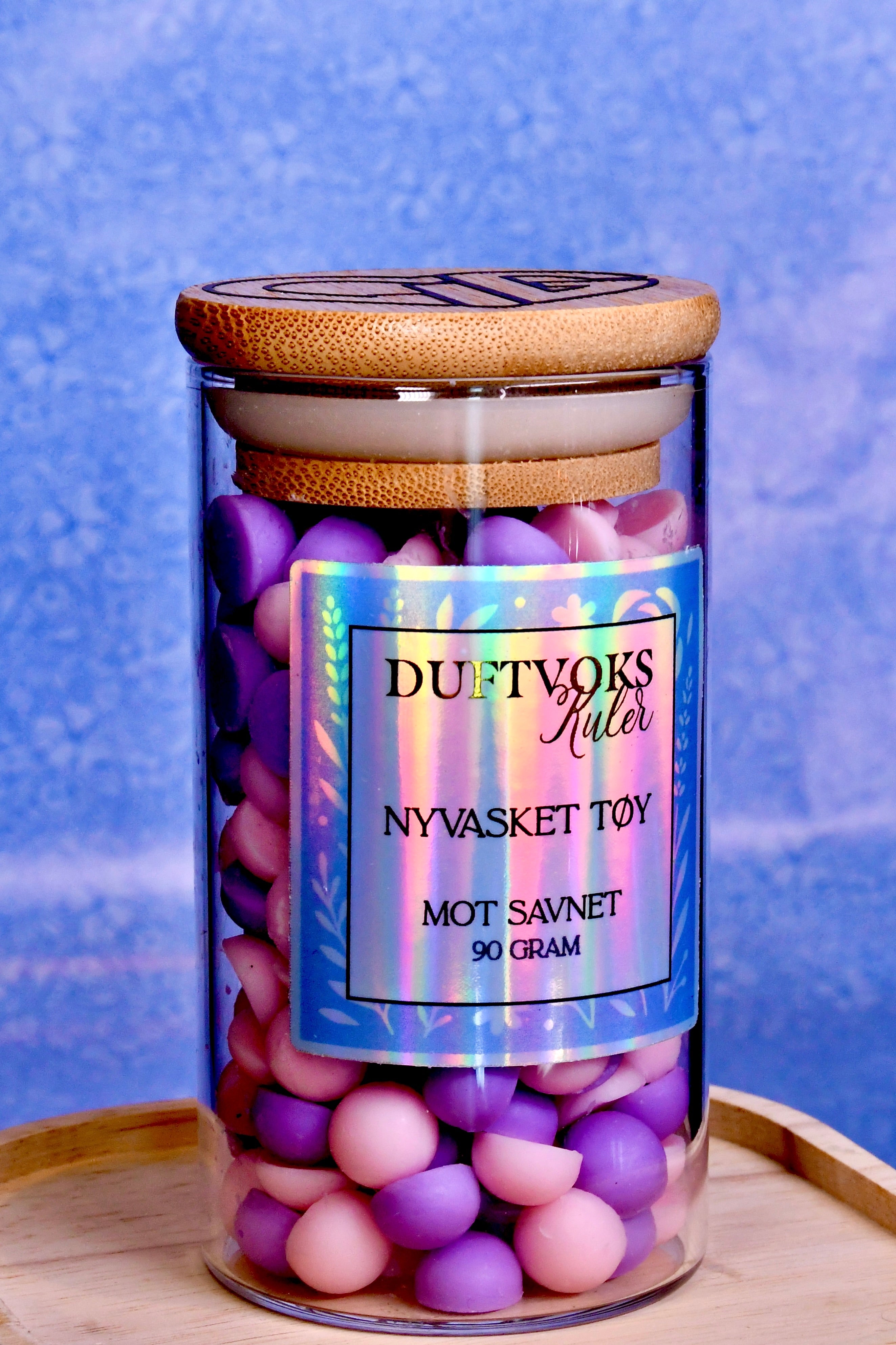 Duftvoks i glasskrukke. Duftkulene er rosa og lilla og lukter nyvasket klær. En rein og herlig lukt som fyller huset når du savner noen ekstra mye en dag. 
