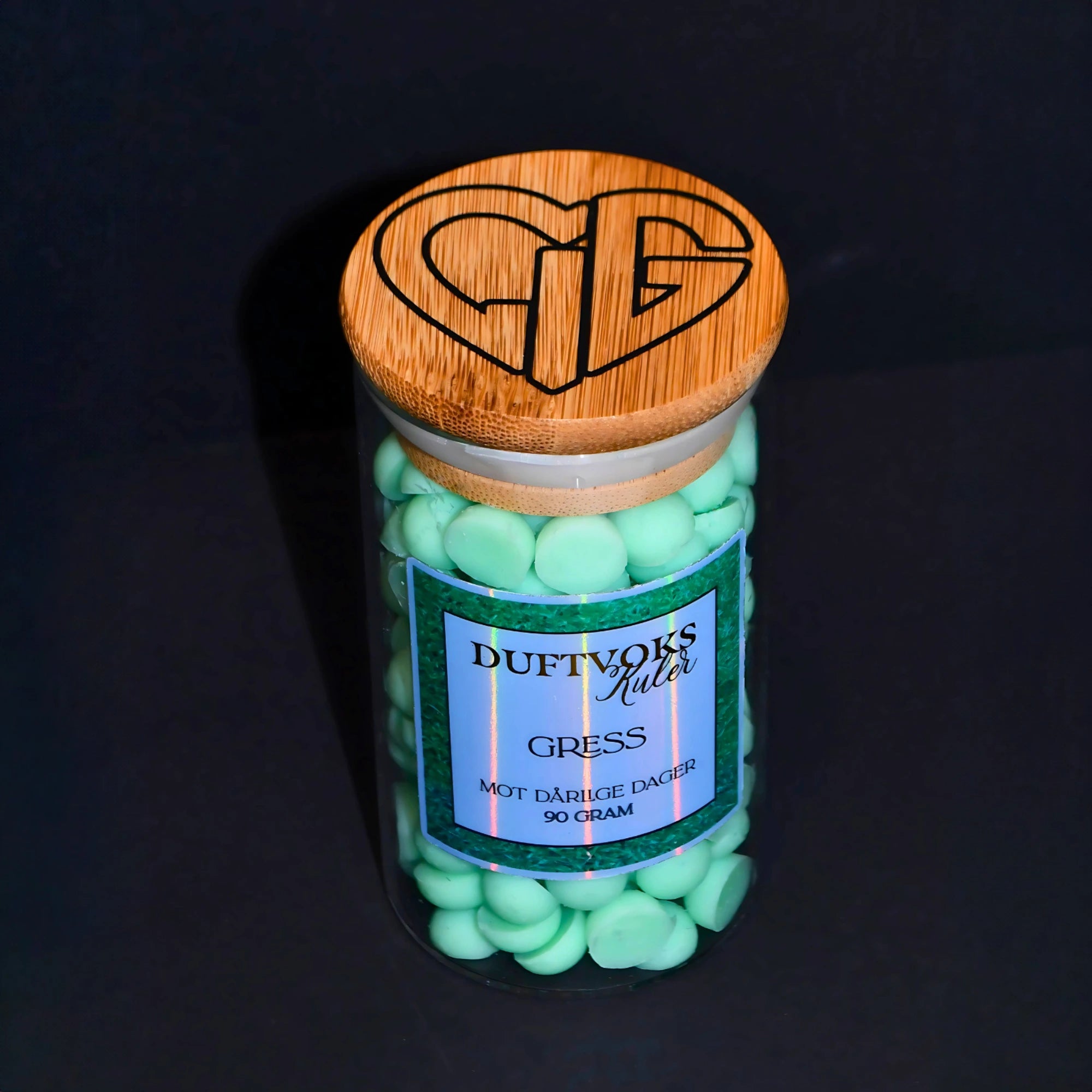På toppen av glasset har vi hjertelig logoen. Duftvokskulene er laget av soyavoks og er håndlaget i Norge. Duften av  nyklipt gress. En frisk duft mot dine dårlige dager som føles tunge.