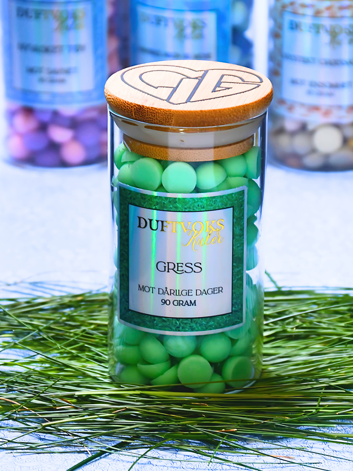 Duftvokskuler som lukter gress. Her står glasskrukken på gress, og man kan se hjertelig logoen på toppen av glasset. Perfekt gave til noen som kanskje ikke har det så bra akkurat nå. 