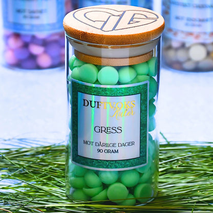 Duftvokskuler som lukter gress. Her står glasskrukken på gress, og man kan se hjertelig logoen på toppen av glasset. Perfekt gave til noen som kanskje ikke har det så bra akkurat nå. 